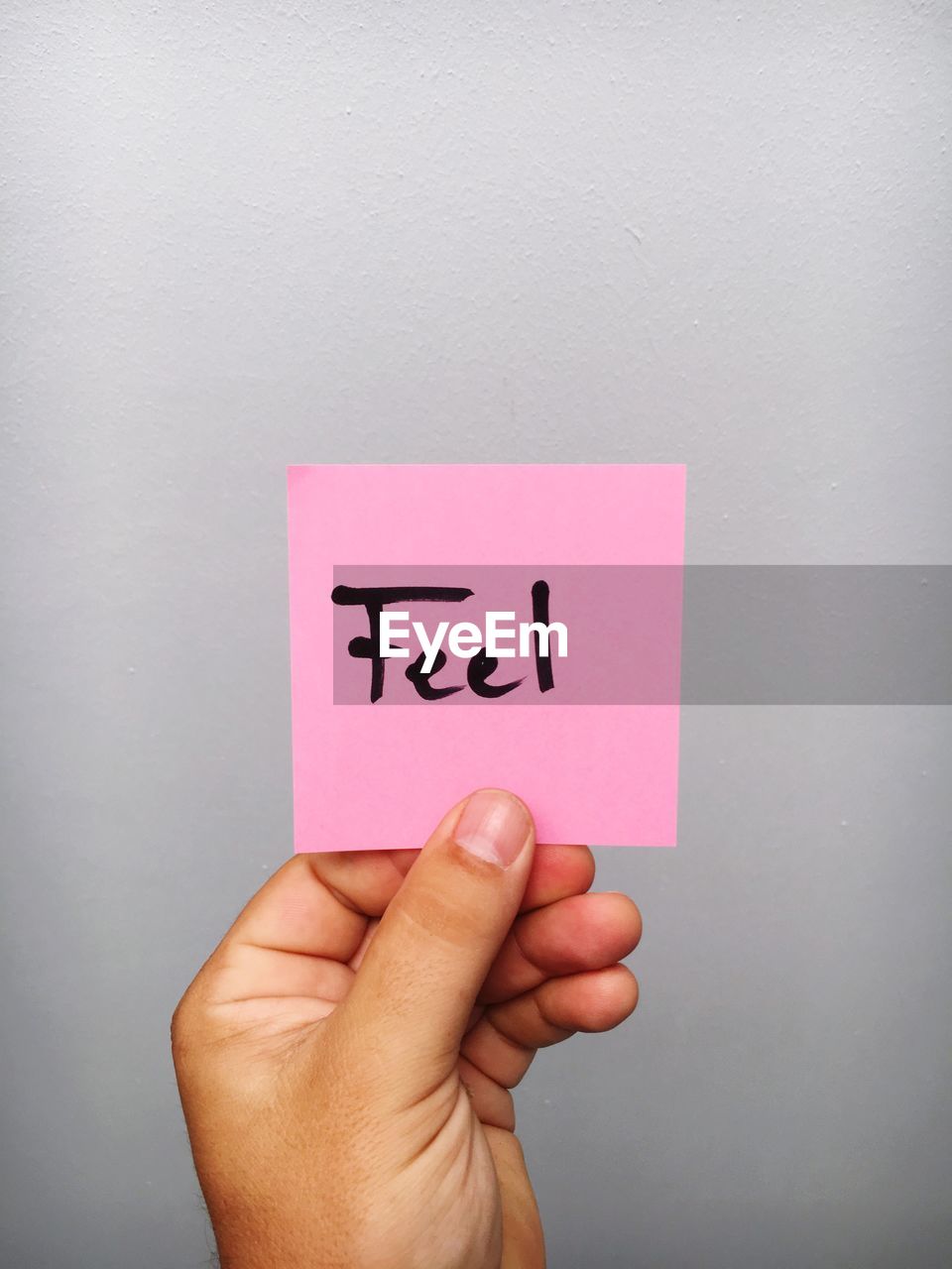 Cropped hand of person holding feel text on adhesive note against gray background