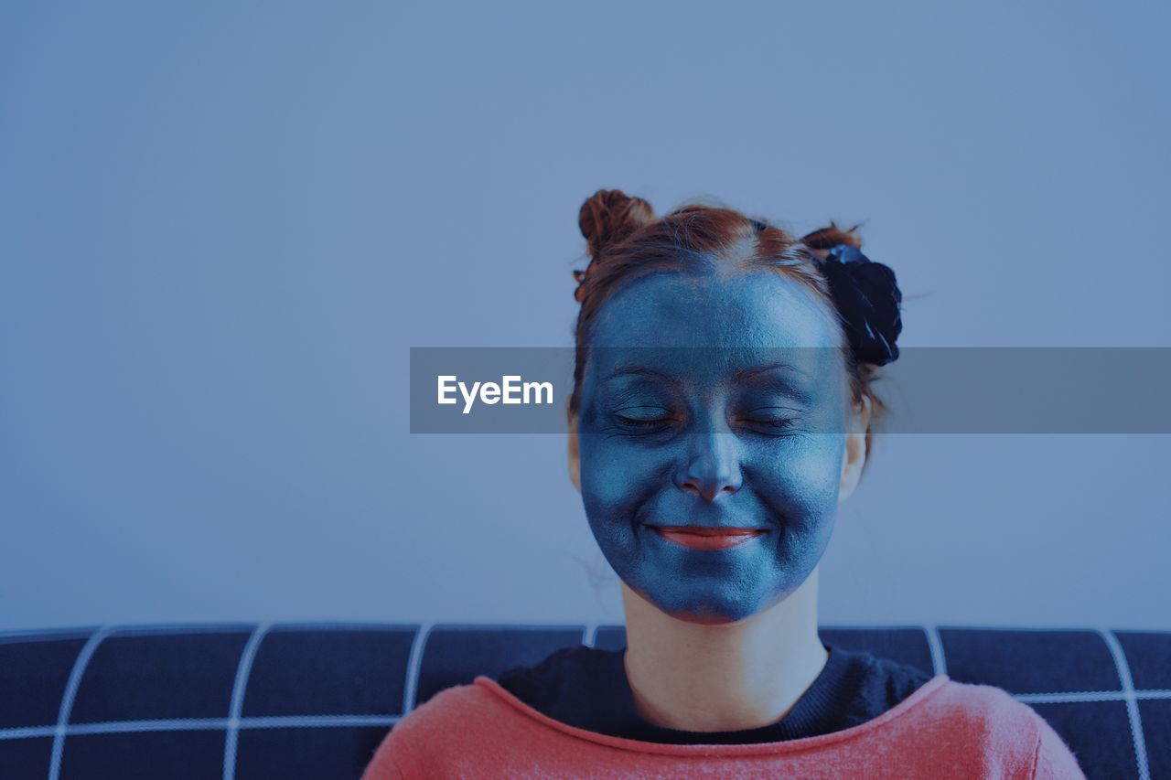 Close-up of young woman with beauty mask against blue wall