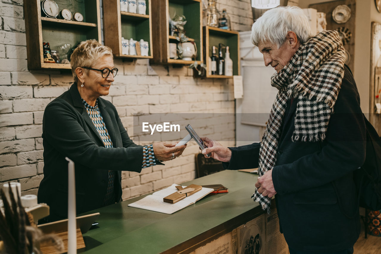 Senior male customer paying via tap to pay at checkout counter in home decor shop