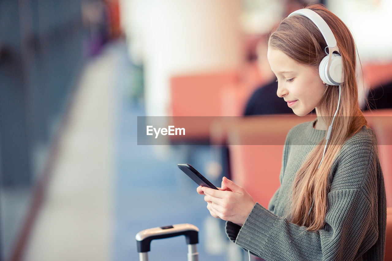 Side view of girl using mobile phone while standing at airport