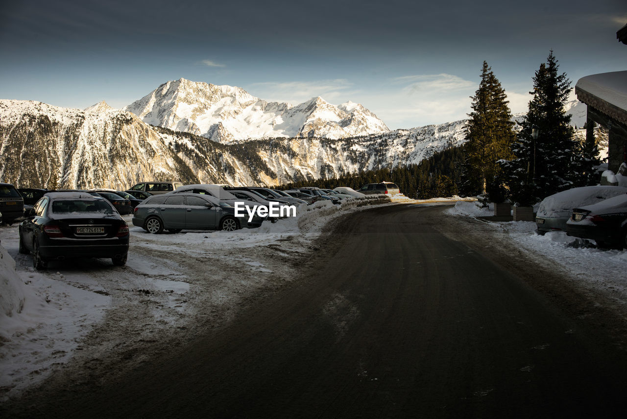 Cars on field by road against snowcapped mountains