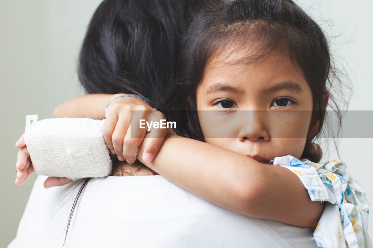 Mother carrying sick daughter against wall in hospital