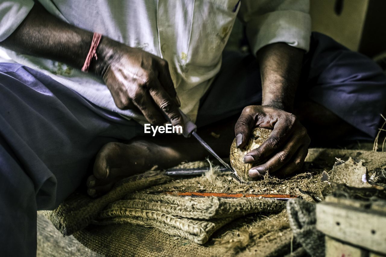 Midsection of man cutting coconut on burlap