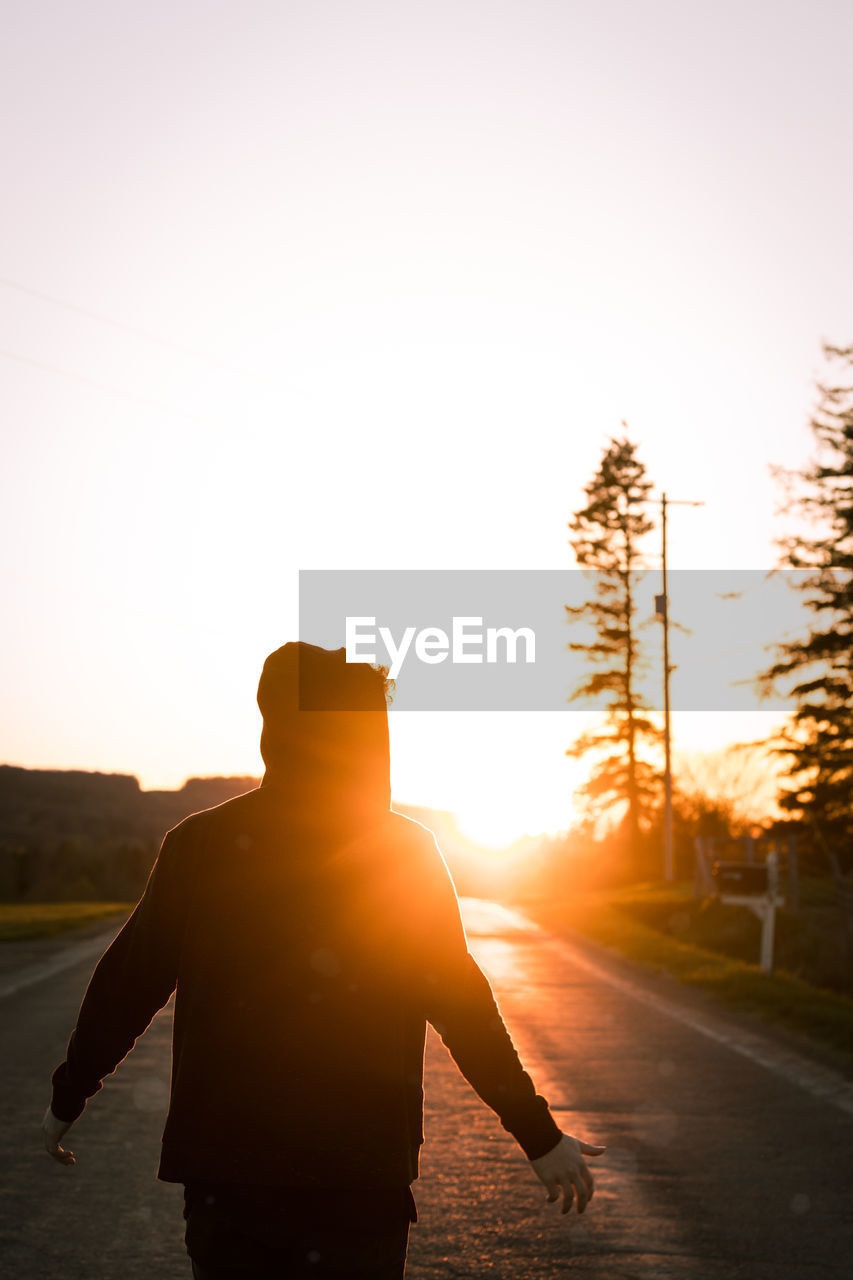 Rear view of silhouette man standing on road against sky during sunset
