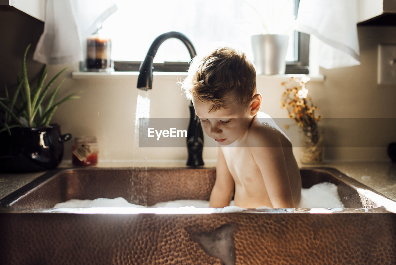 Shirtless boy taking bath while sitting in sink at home