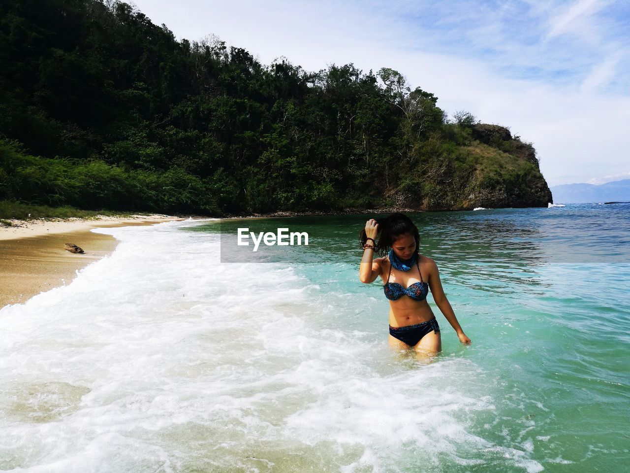 Woman wearing bikini while standing in sea against mountain