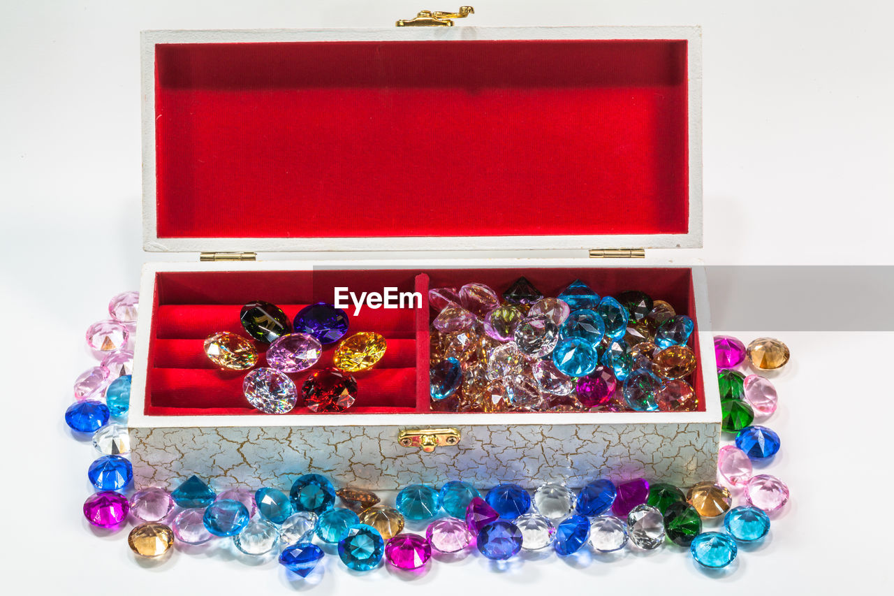 Close-up of colorful gemstones and box over white background