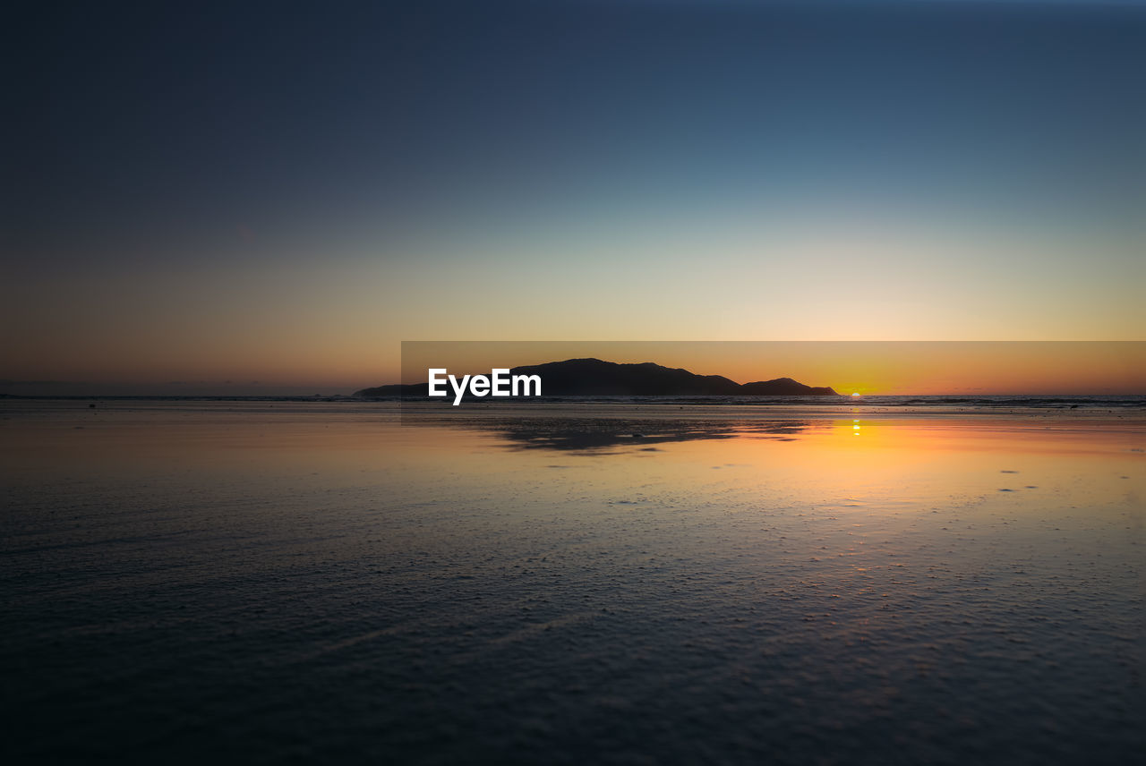 SCENIC VIEW OF BEACH AGAINST CLEAR SKY DURING SUNSET