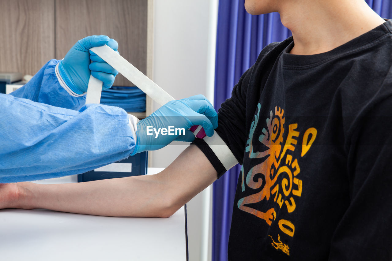 Nurse tightening the elastic band on a male patient arm to collect a blood sample from in a clinic