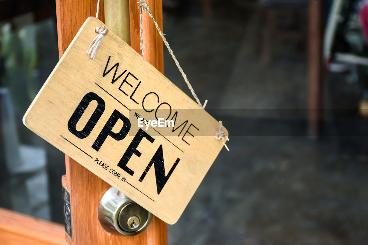 Close-up of open sign with text hanging on door at cafe