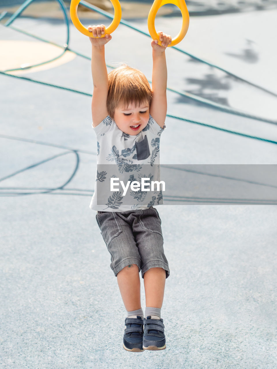 Little boy is training on public sports ground. kid is doing exercises on sport rings. 