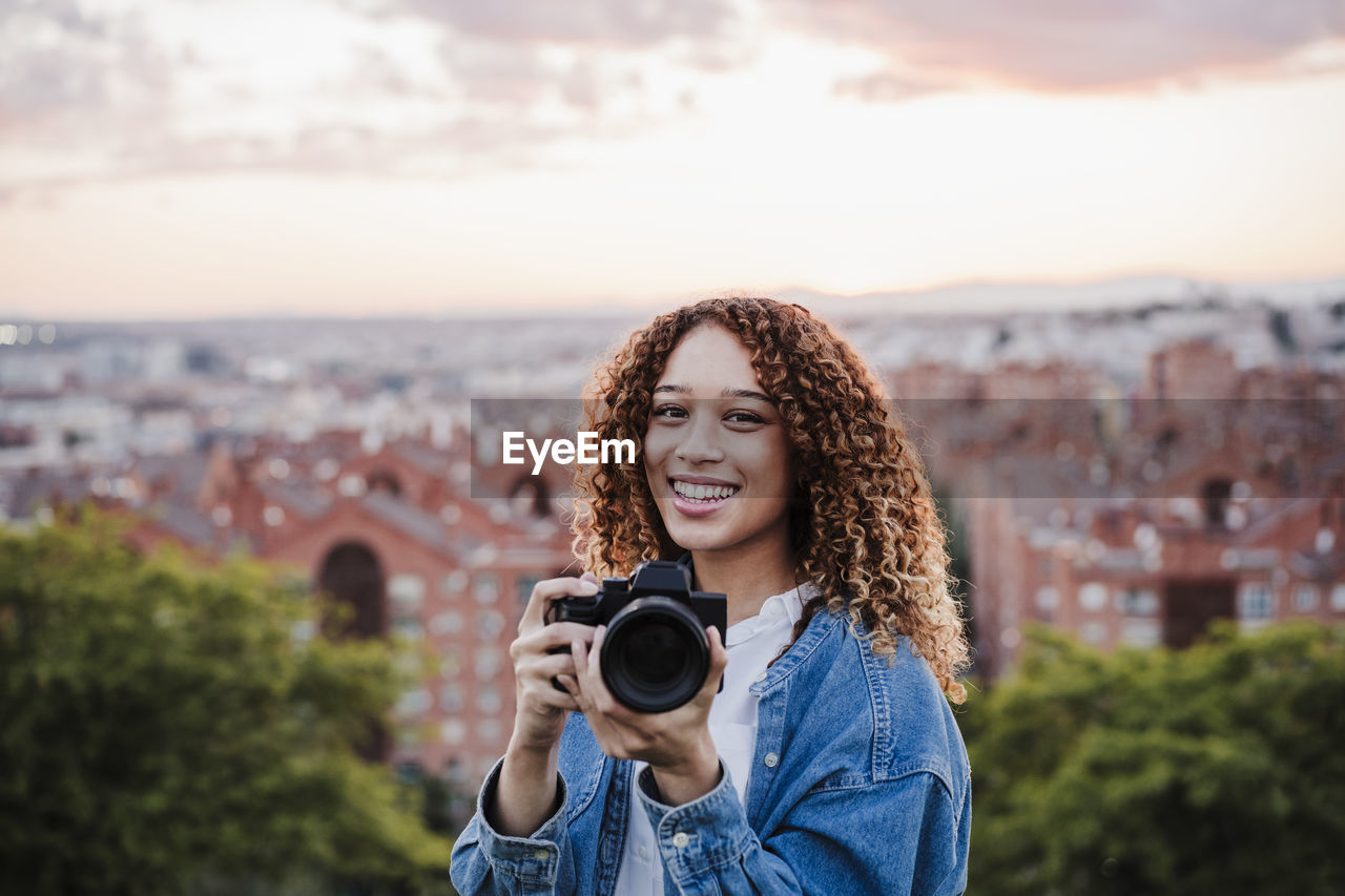 Smiling woman holding camera during sunset