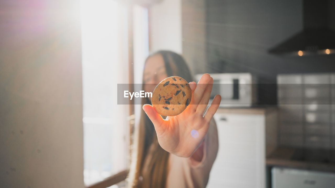 Young female with delicious oatmeal cookie with chocolate chips at home on sunny day