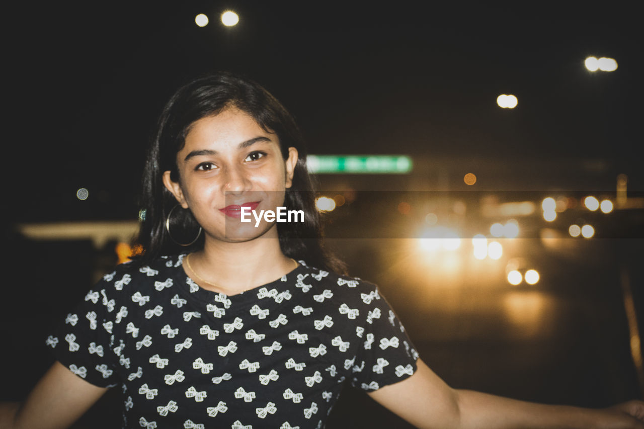 Portrait of smiling teenage girl standing in city at night