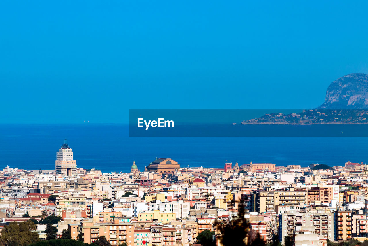 Aerial view of townscape by sea against blue sky