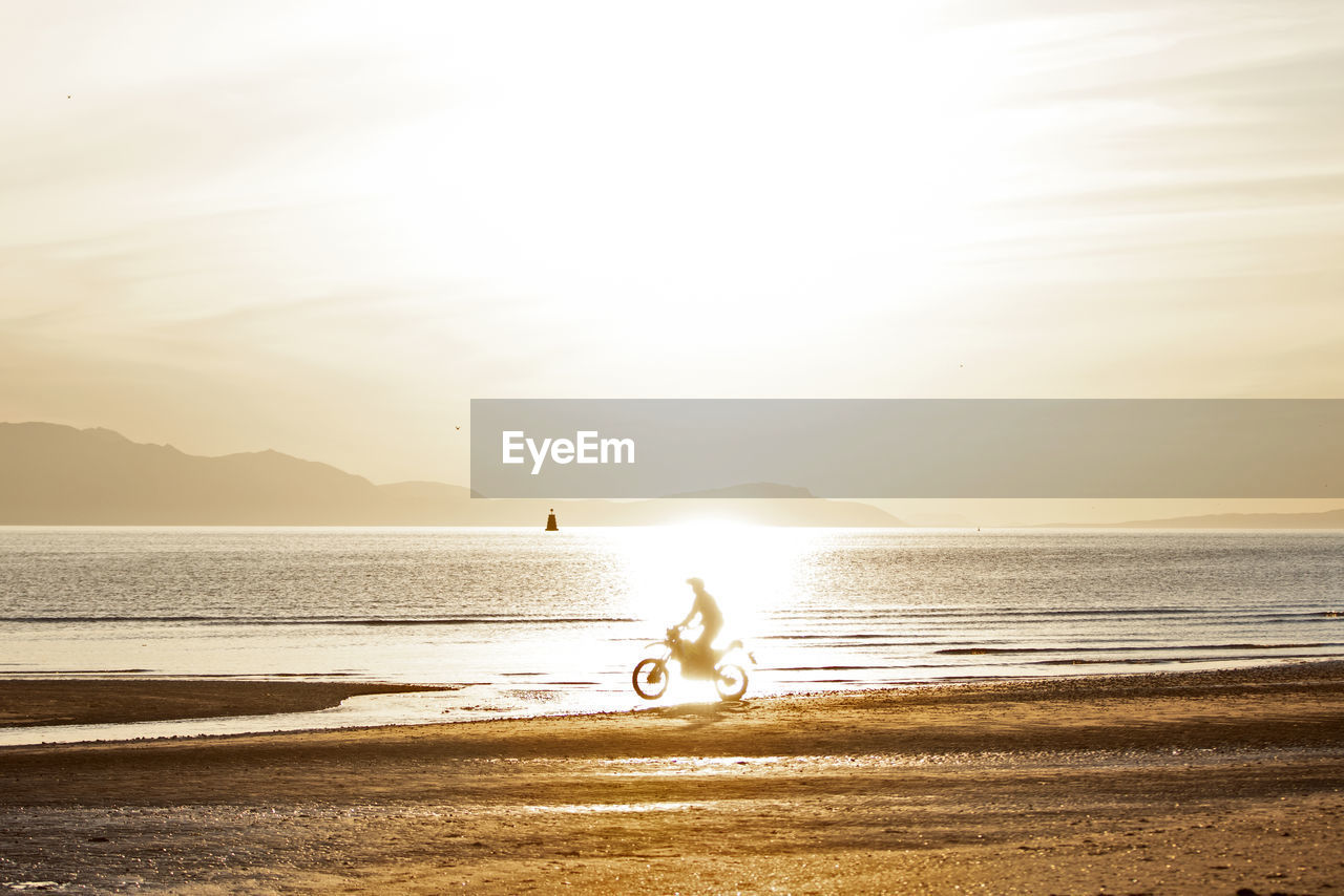 MAN RIDING BICYCLE ON BEACH