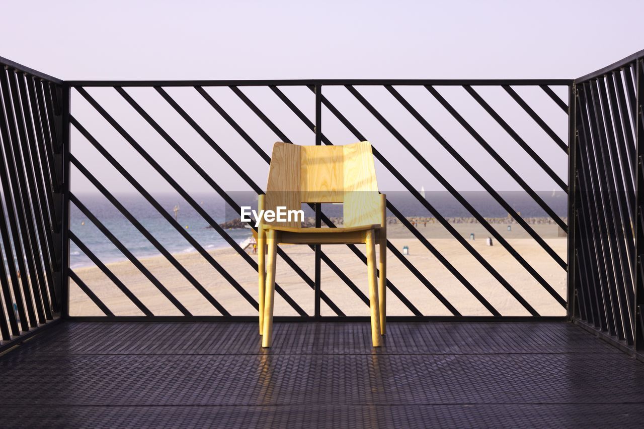 Close-up of chair on by fence against sea