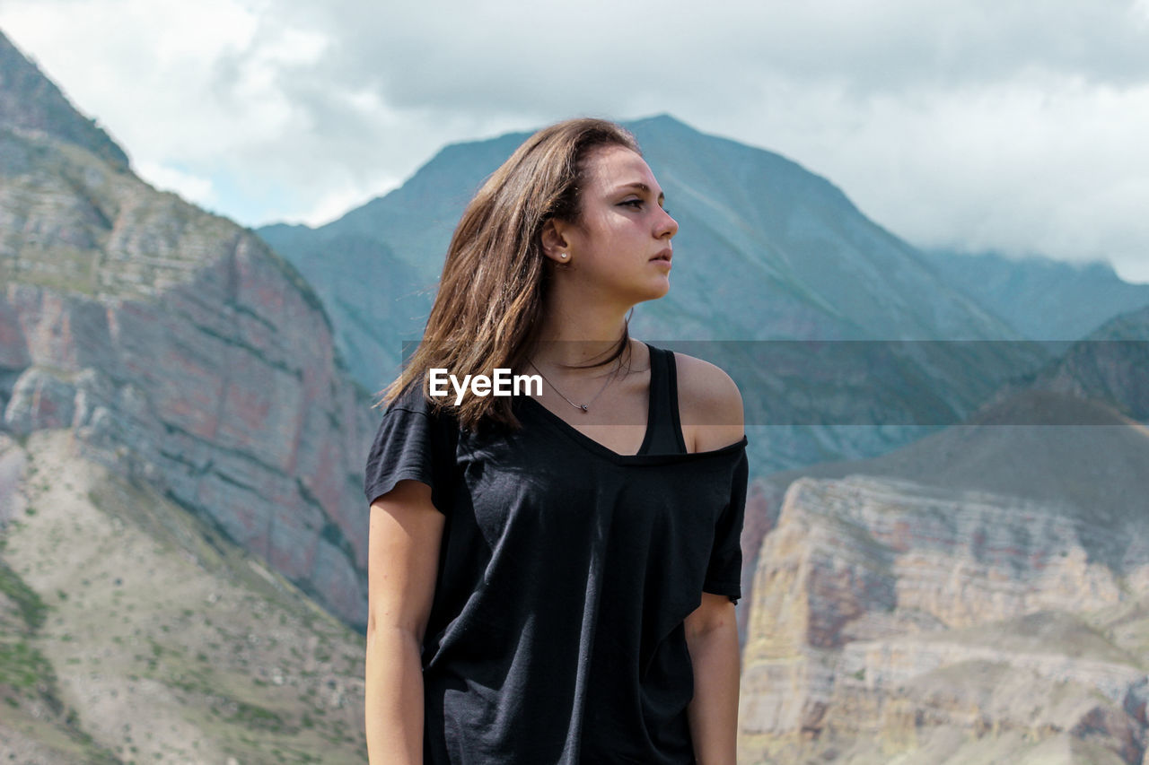 Beautiful young woman looking away while standing against mountain range