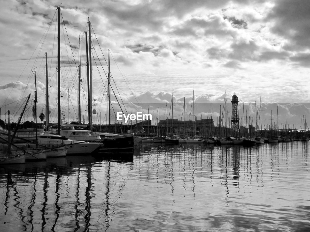 SAILBOATS MOORED IN HARBOR AGAINST SKY IN CITY