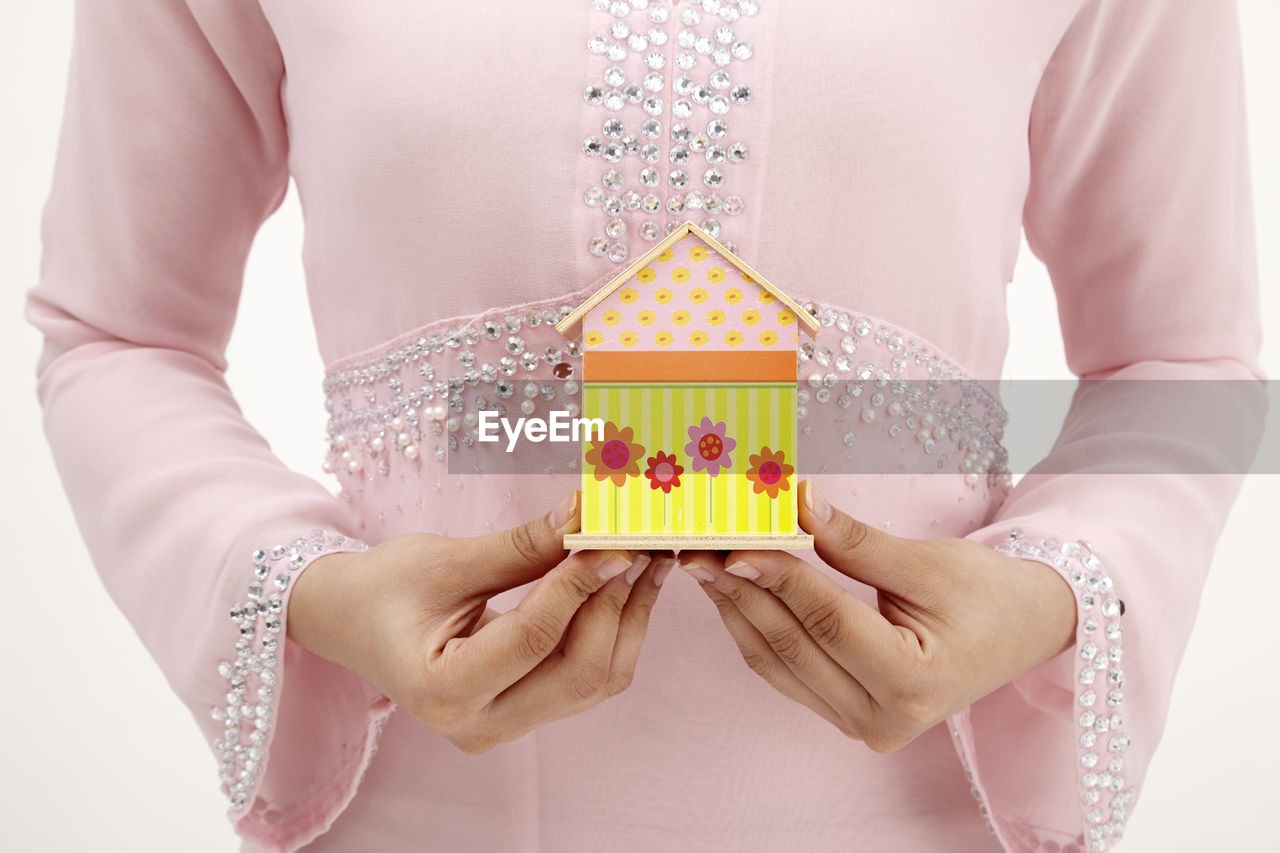 Midsection of woman holding model home against white background