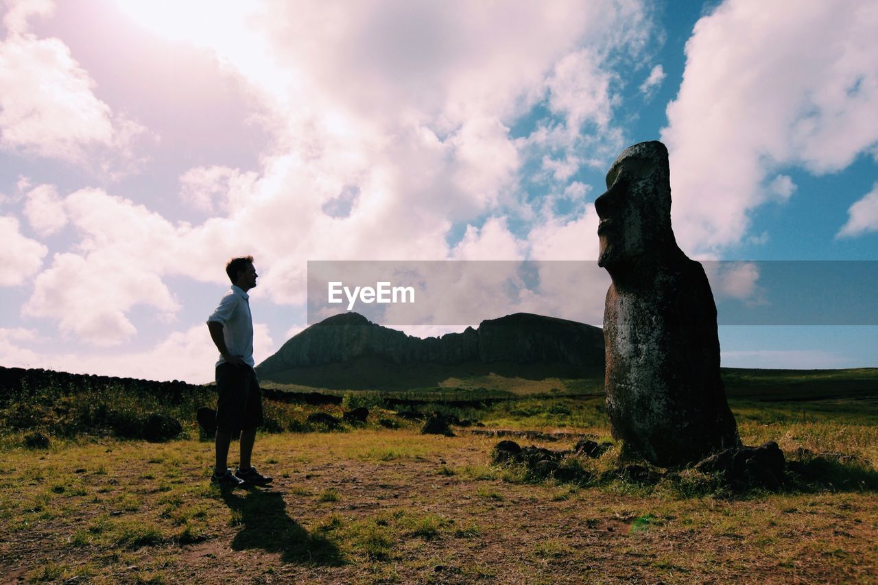 Man standing in front of moai statue on field against sky at easter island