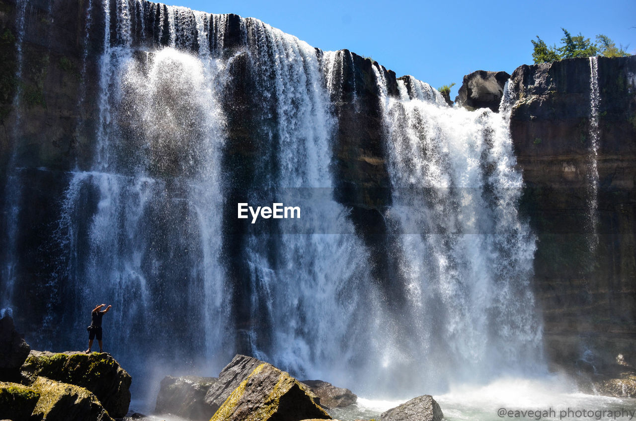 Scenic view of waterfall with man standing on rock