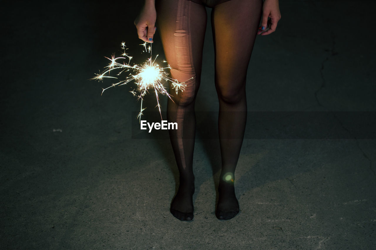 Low section of woman with sparkler standing on walkway at night