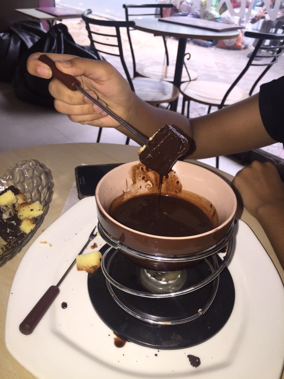 Cropped image of hand dipping cake in chocolate fondue