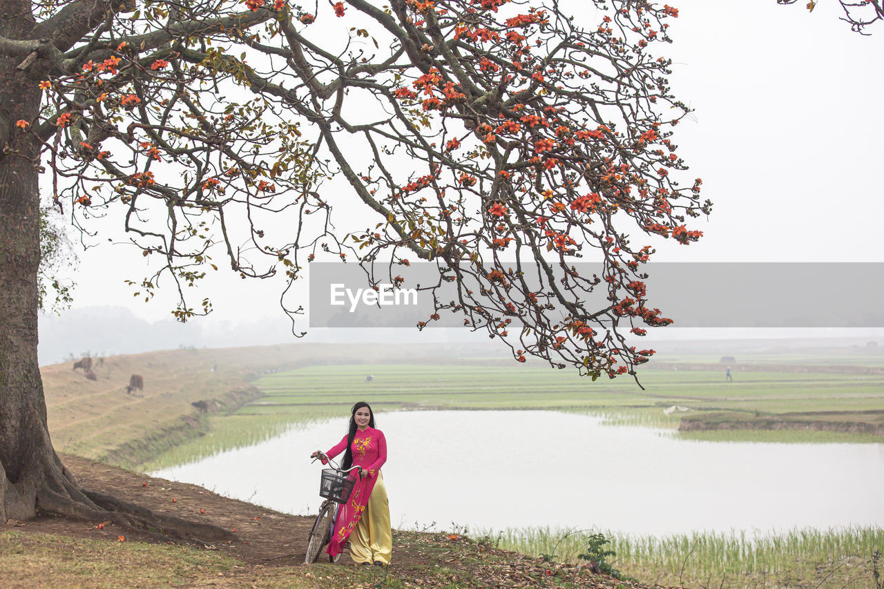 plant, tree, flower, nature, adult, landscape, one person, beauty in nature, environment, sky, tranquility, rural scene, water, land, clothing, women, full length, scenics - nature, outdoors, day, field, lake, traditional clothing, tranquil scene, red, grass, blossom, men, tradition, fog, non-urban scene, standing, leaf, rural area, autumn