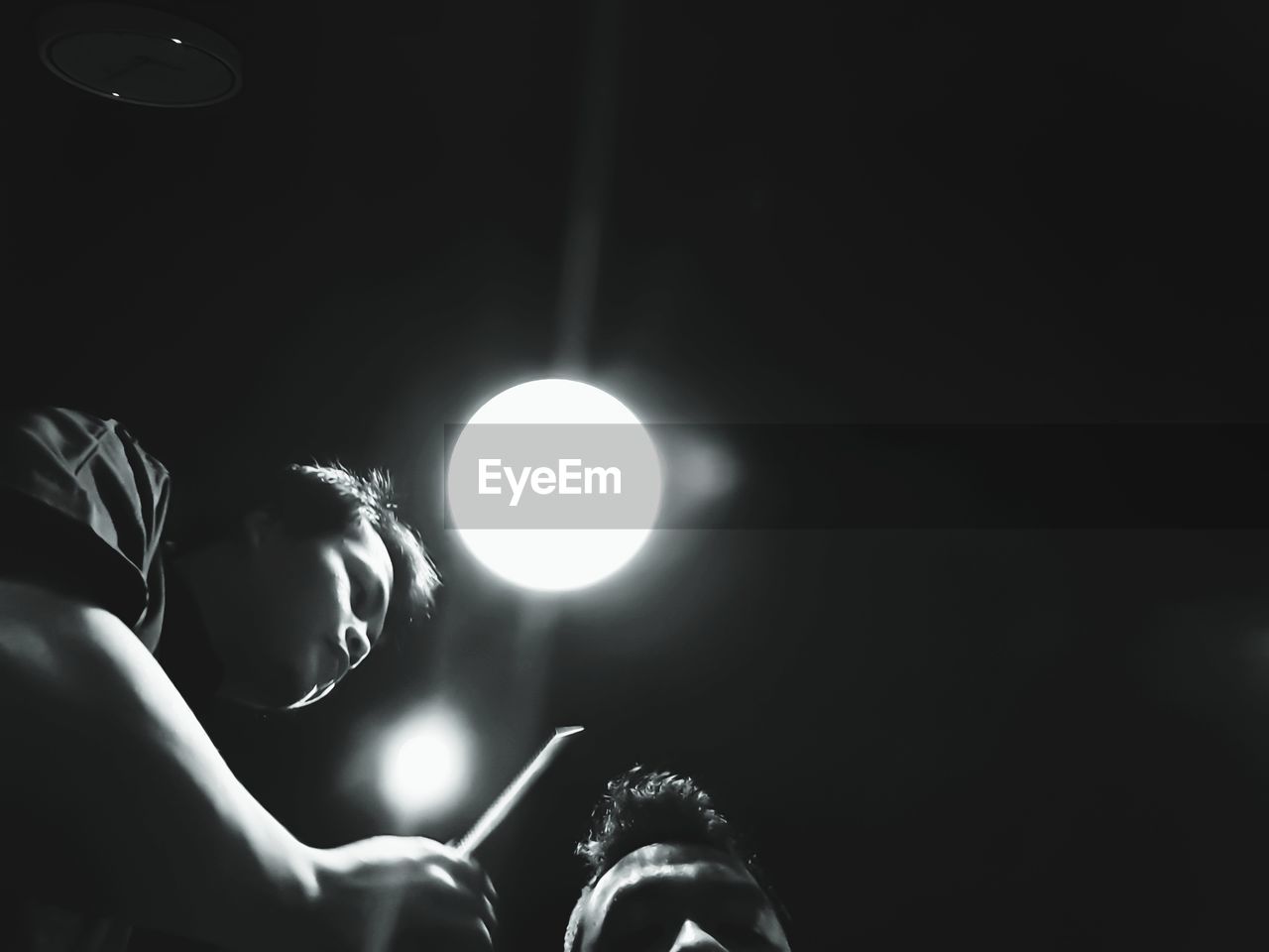 Low angle view of man hairstyling customer in darkroom