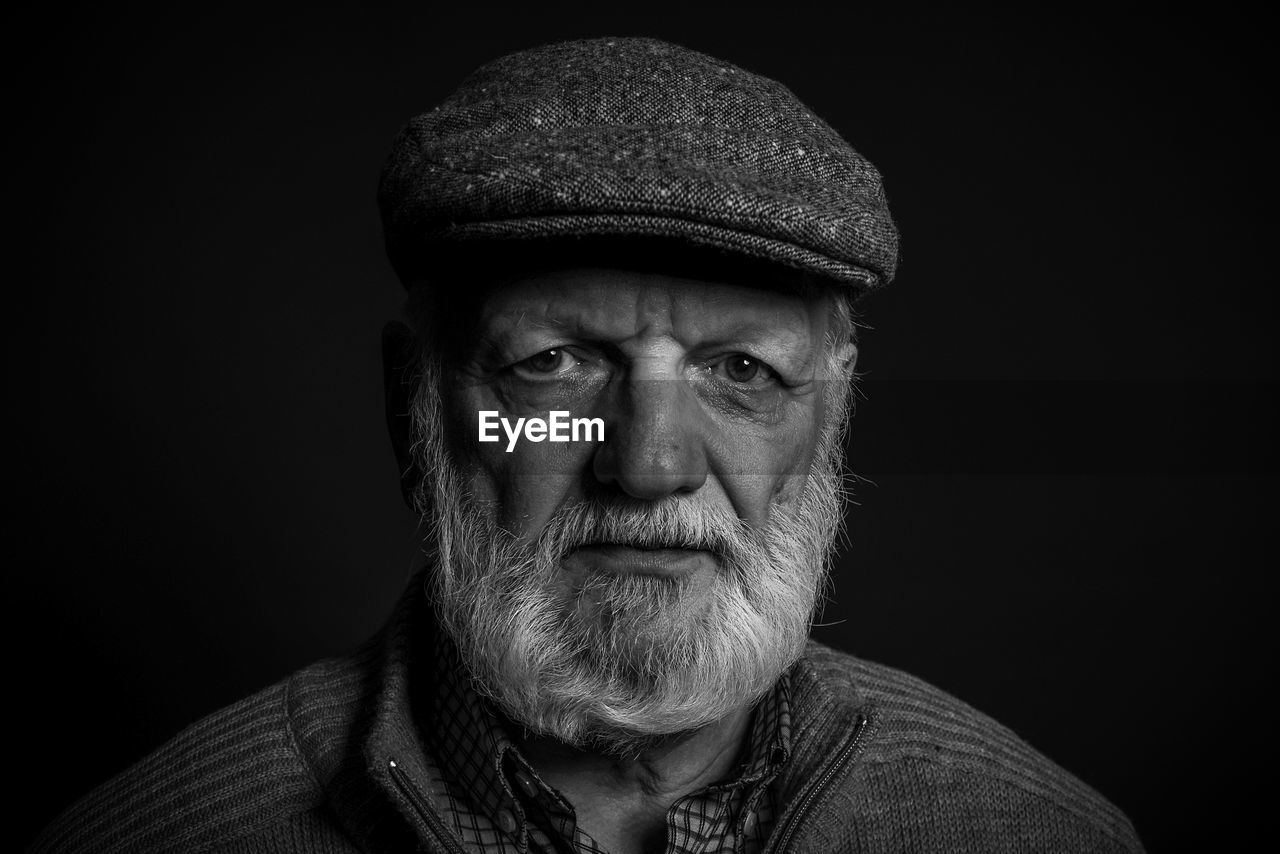 Portrait of old man wearing hat against black background