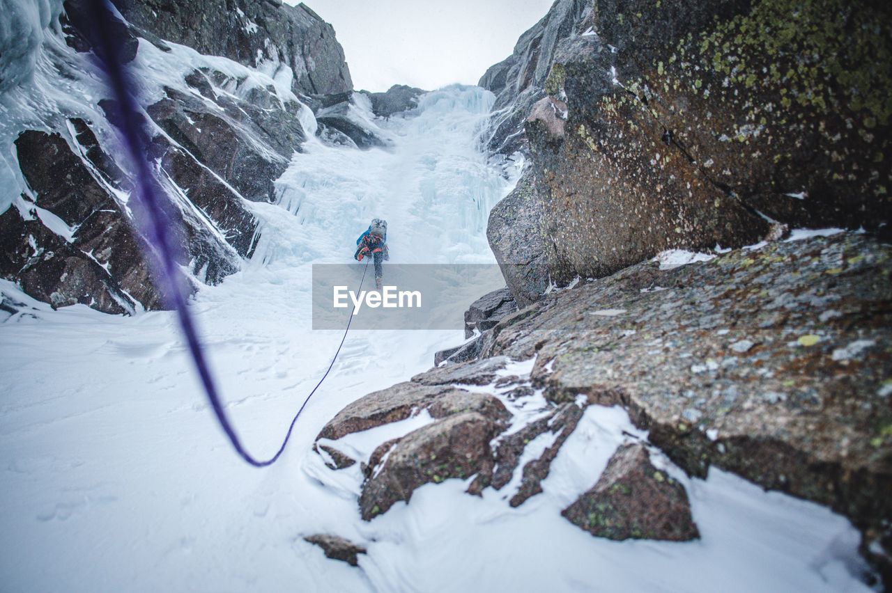 An ice climber climbs up a steep gully full of ice in maine alpine