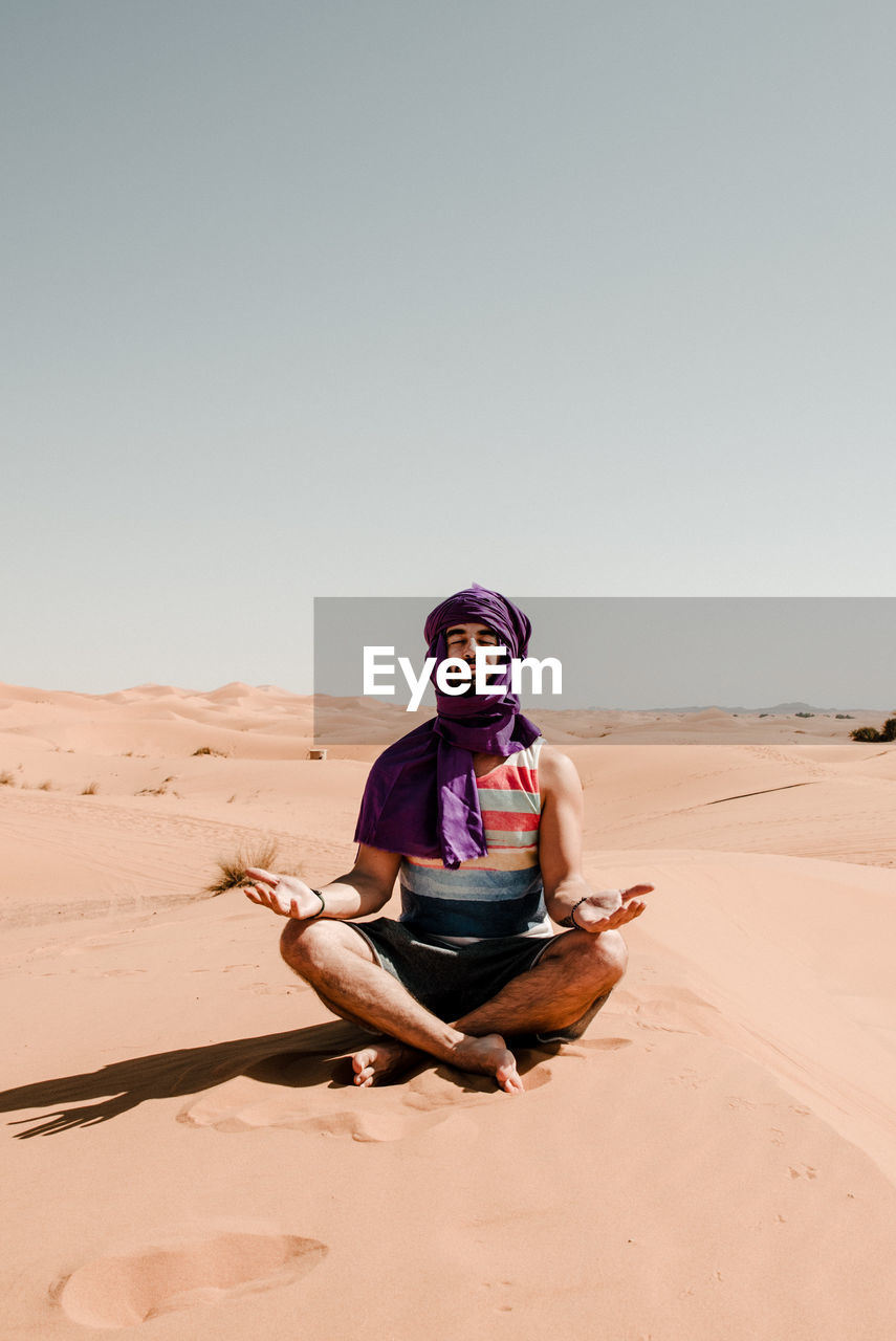 A man in a turban meditating on a dune in the sahara desert