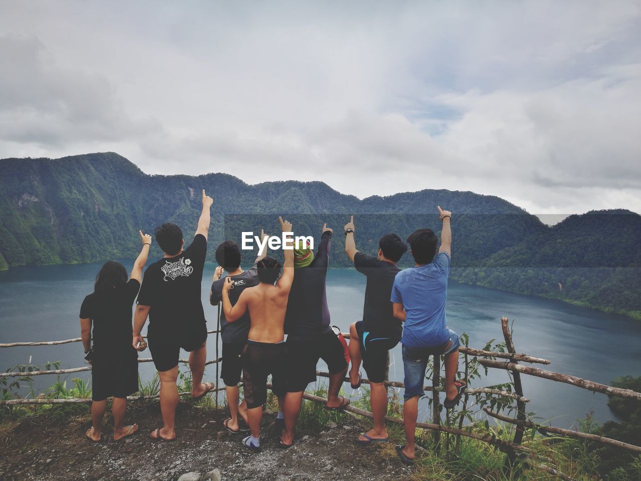 Friends pointing against mountains by lake against cloudy sky