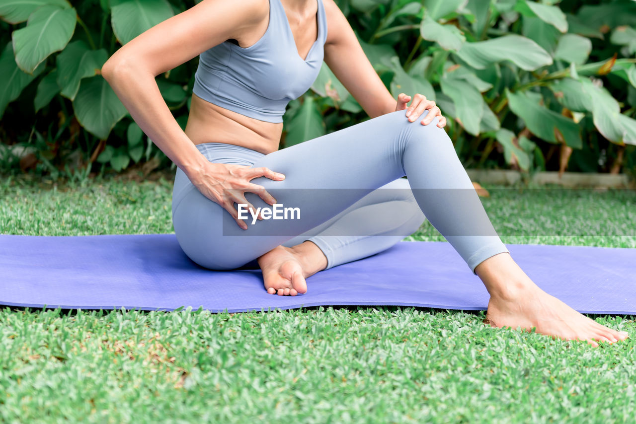 MIDSECTION OF WOMAN SITTING ON GRASSLAND