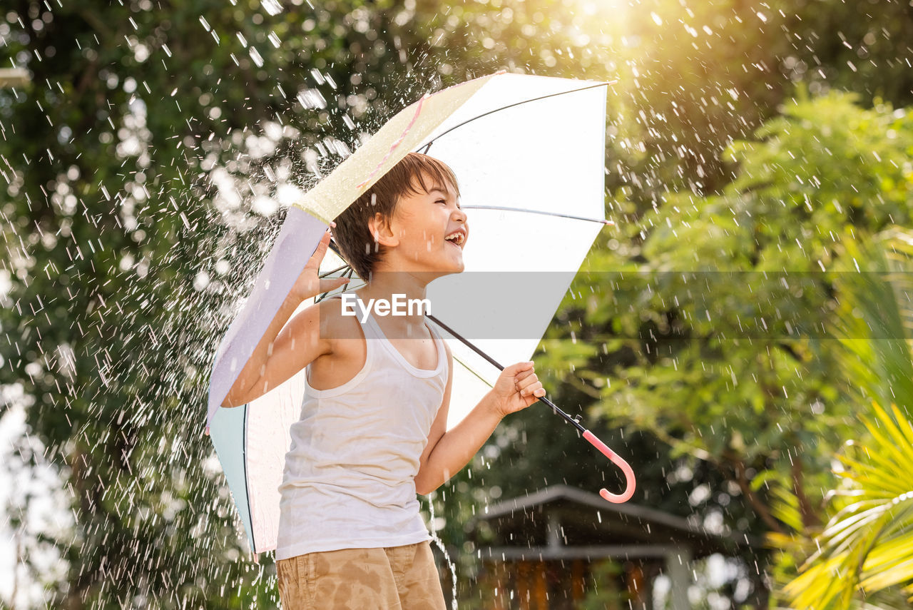 Boy holding umbrella while standing against trees