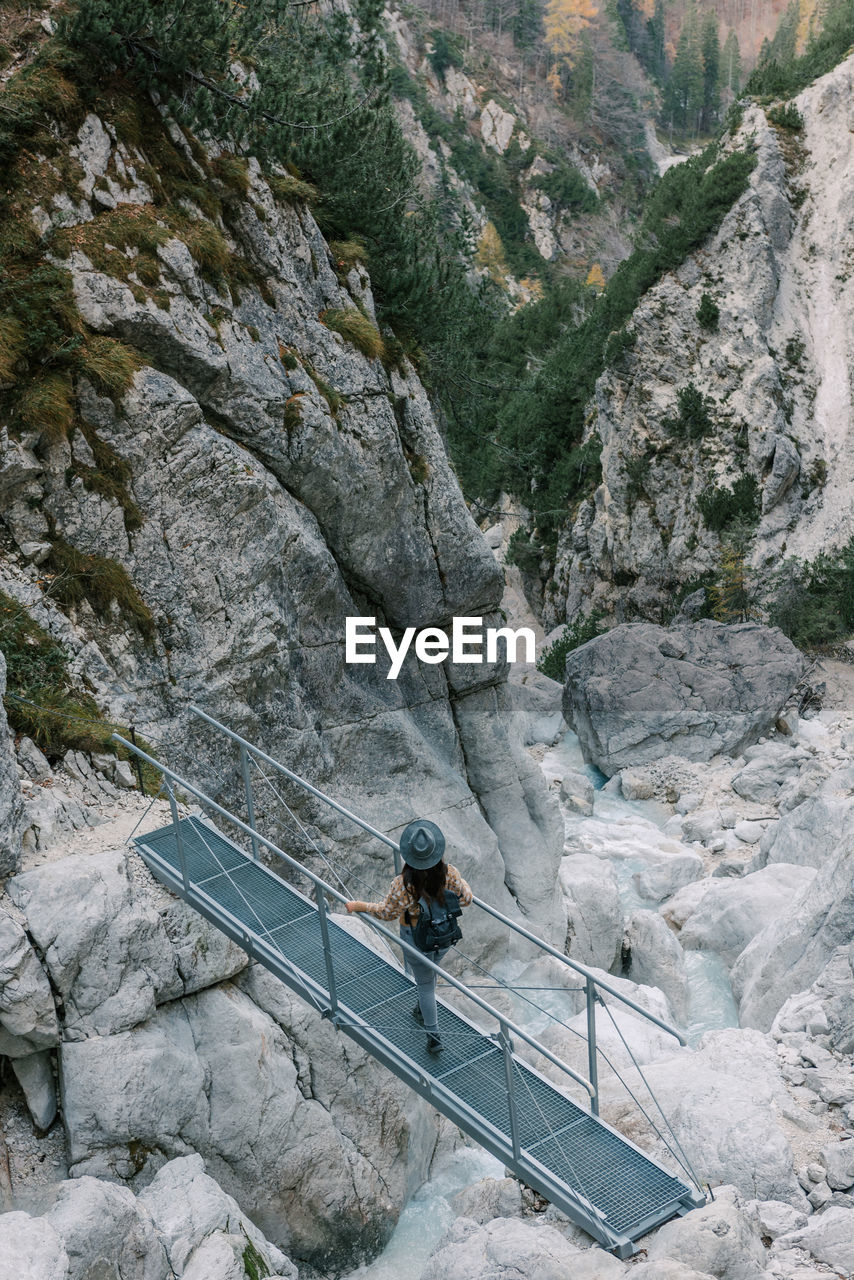 Woman standing on footbridge over mountain torrent, looking at landscape view