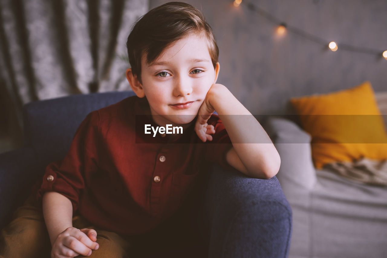 Portrait of smiling cute boy sitting on chair at home