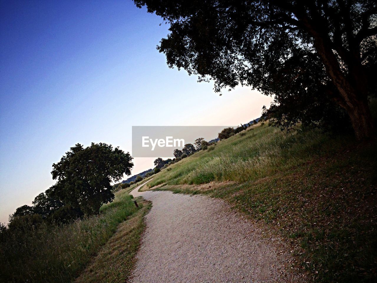 Tilt image of dirt road amidst field against blue sky