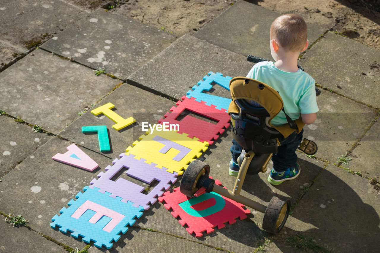 High angle view of boy riding tricycle by text on footpath