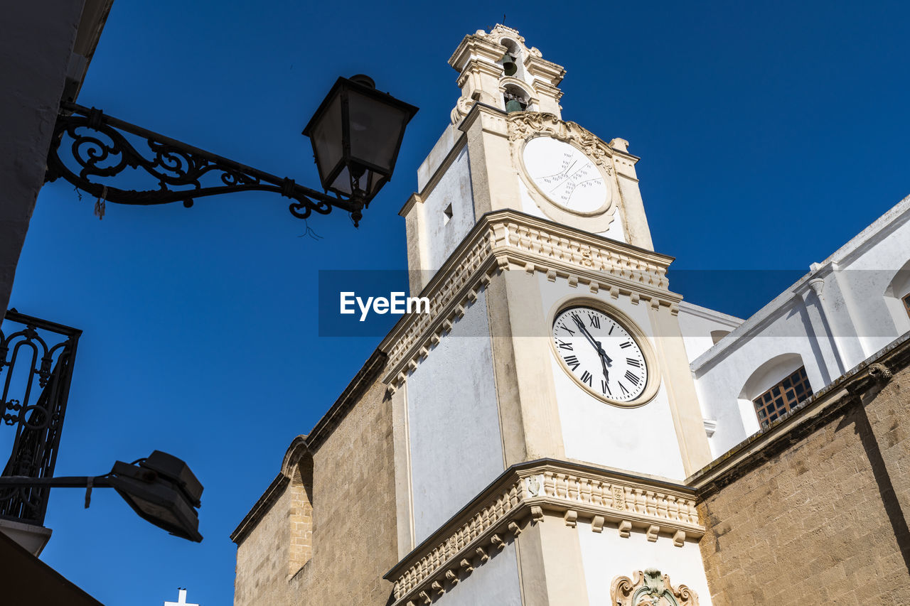 LOW ANGLE VIEW OF CLOCK TOWER AMIDST BUILDING AGAINST SKY