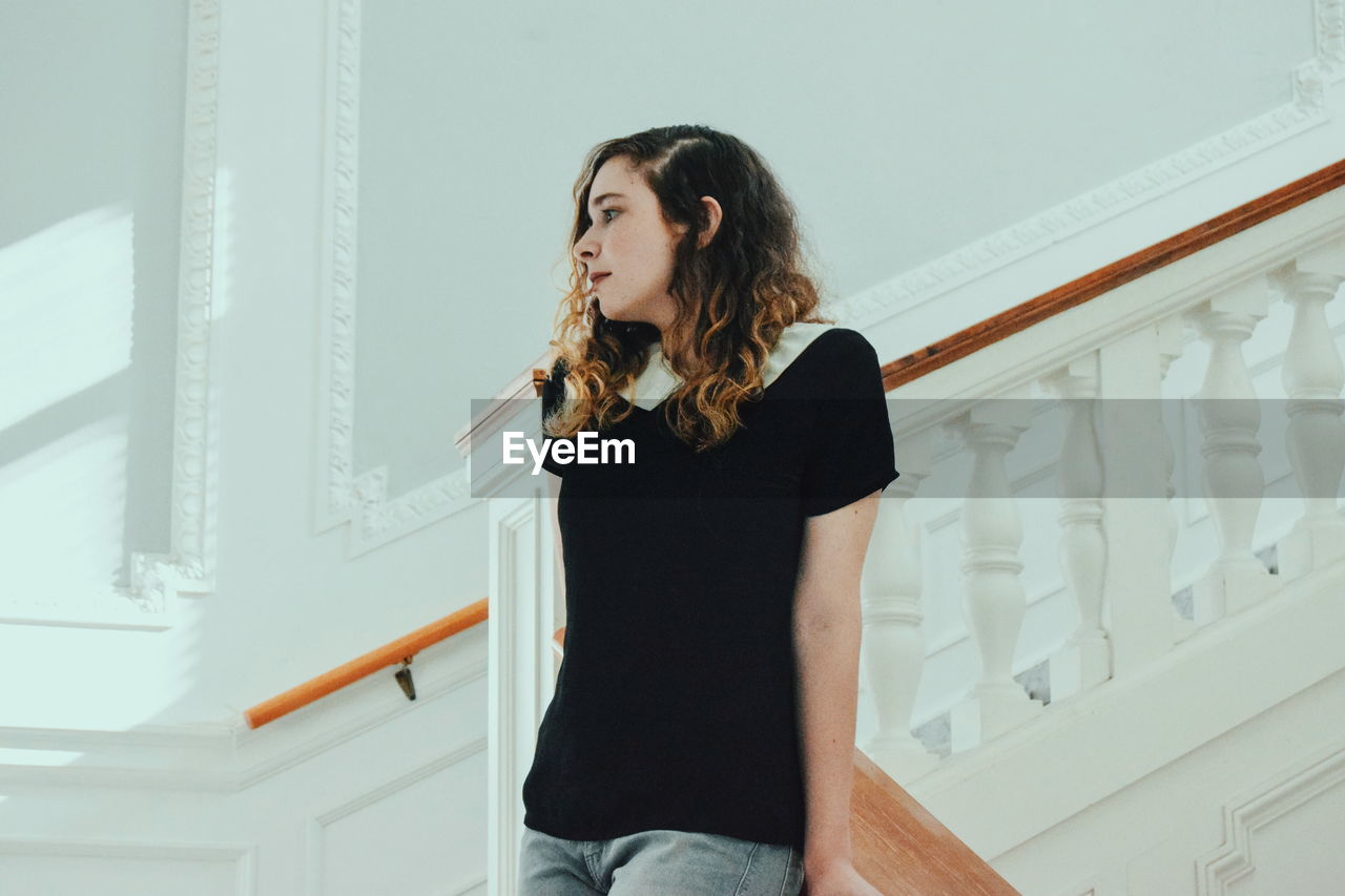 Low angle view of young woman standing on staircase at home