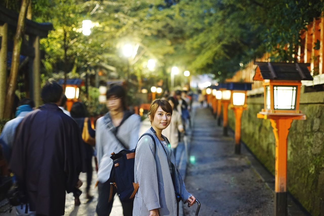 Portrait of woman standing by lamps on footpath at park