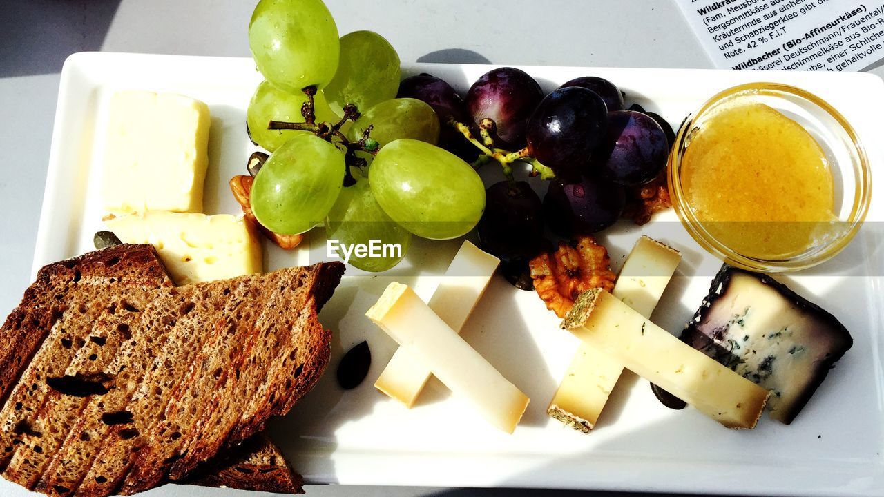 High angle view of cheese with bread and grapes on plate