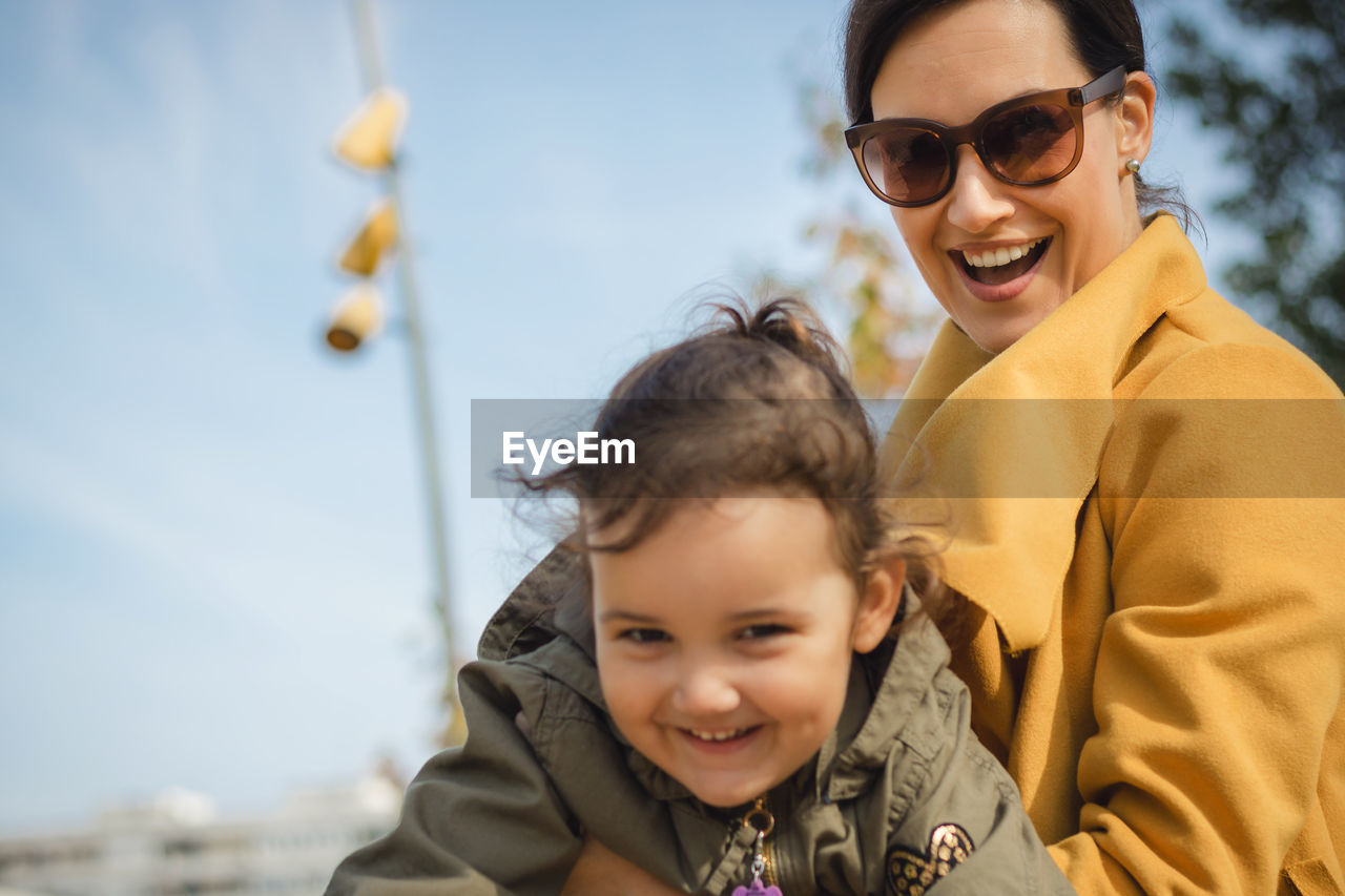 Portrait of smiling mother and daughter against sky