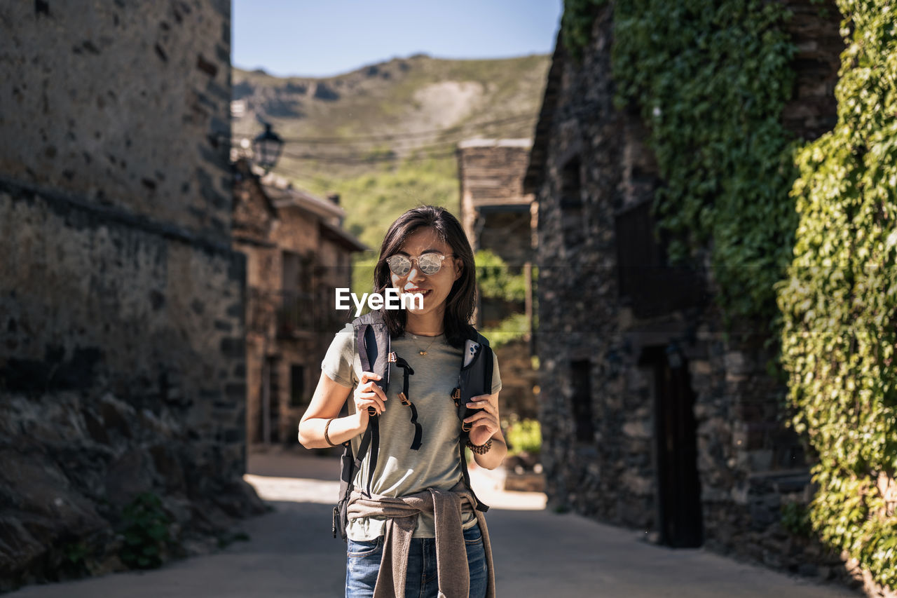 Asian female tourist with backpack standing on street with old stone buildings in province of guadalajara in spain on sunny summer day