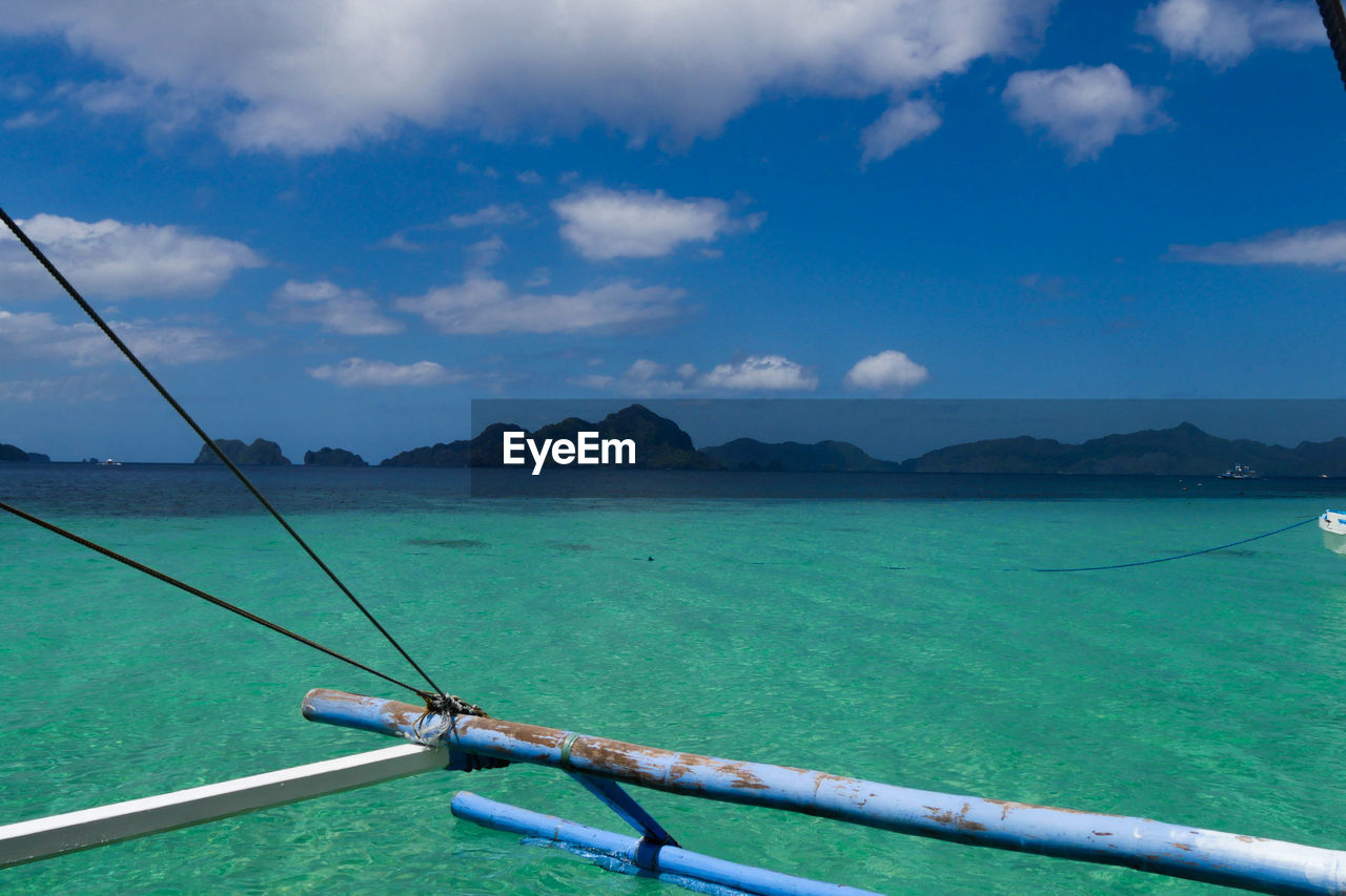 Cropped image of outrigger boat in turquoise sea against sky