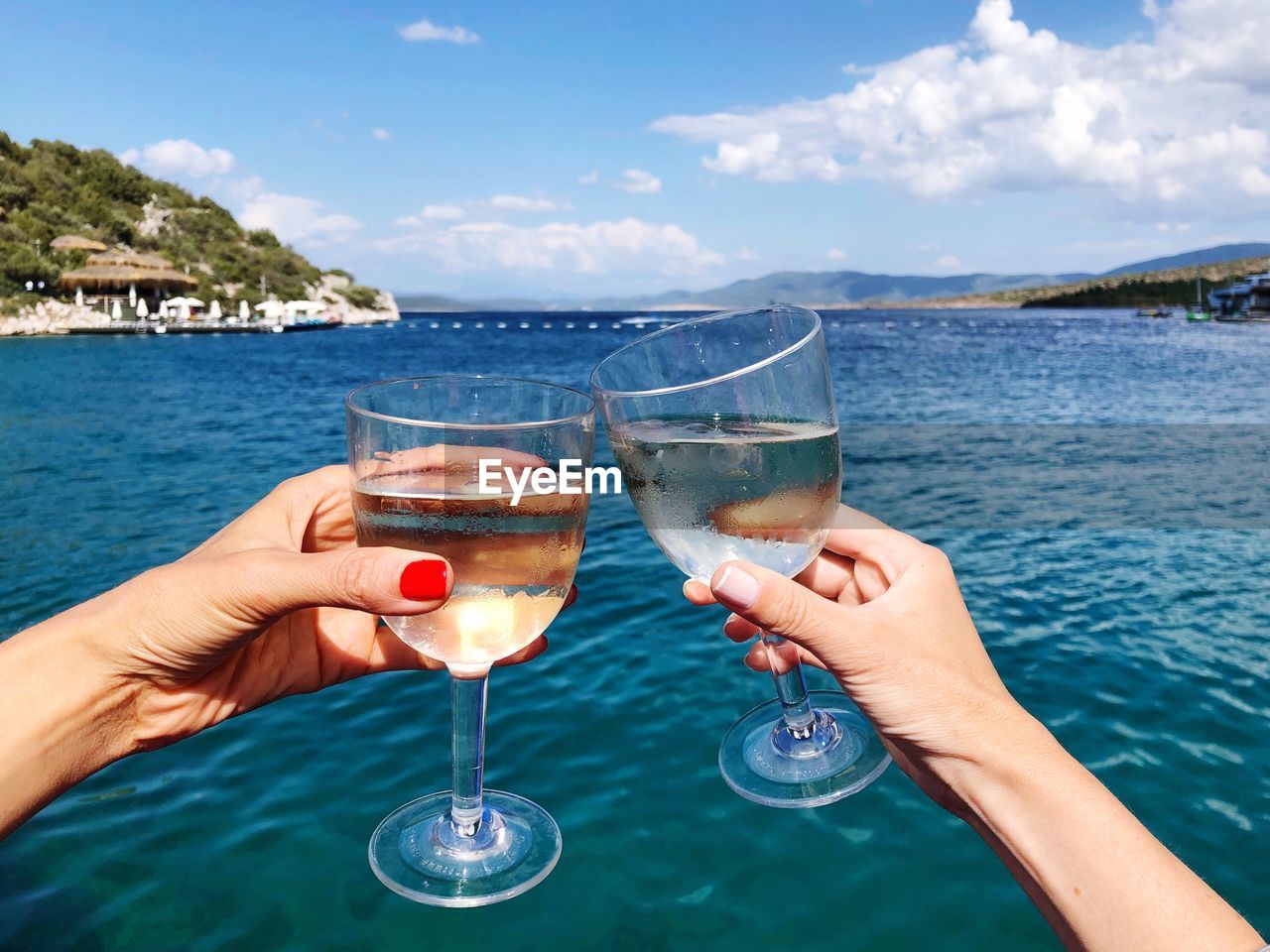 Close-up of hands toasting glass of wine against sky and sea in a sunny day 