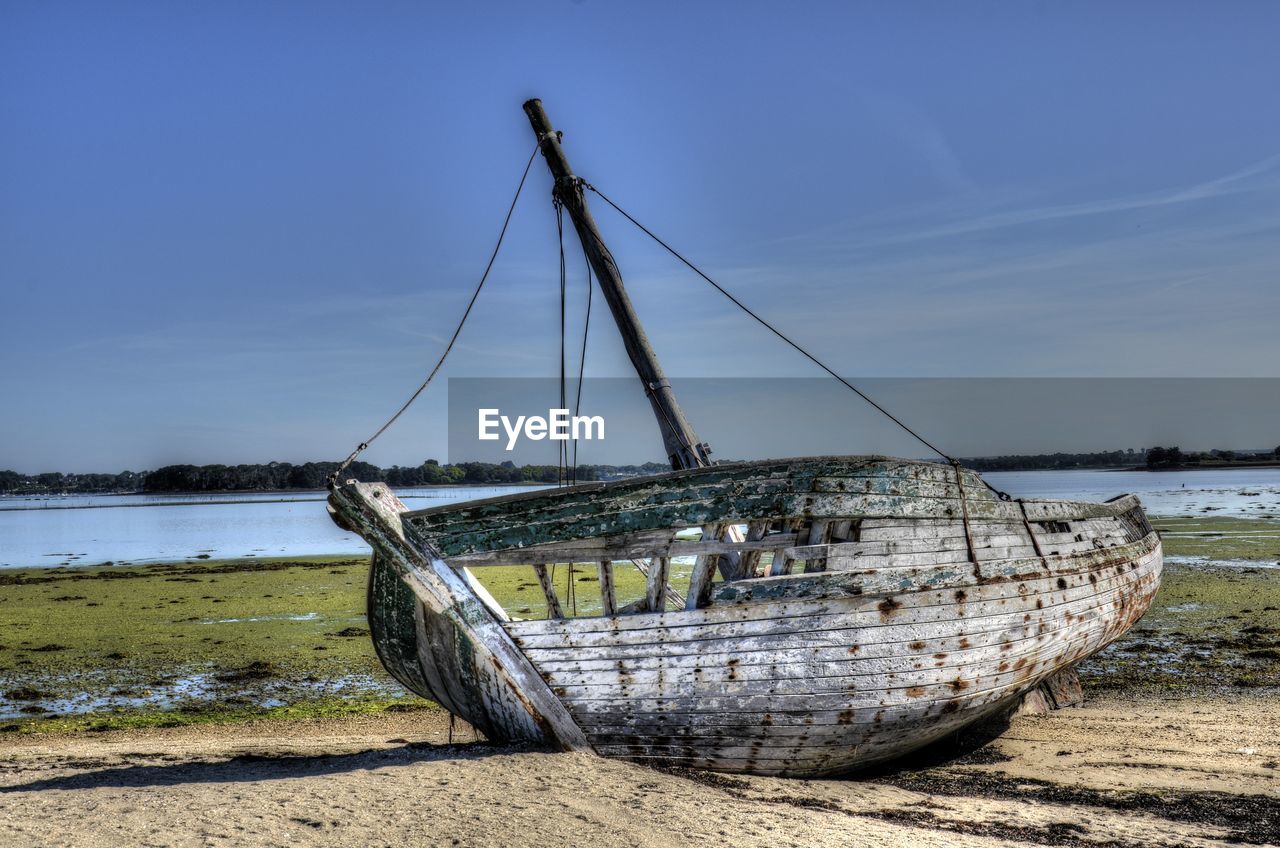 Abandoned boat moored on beach against sky