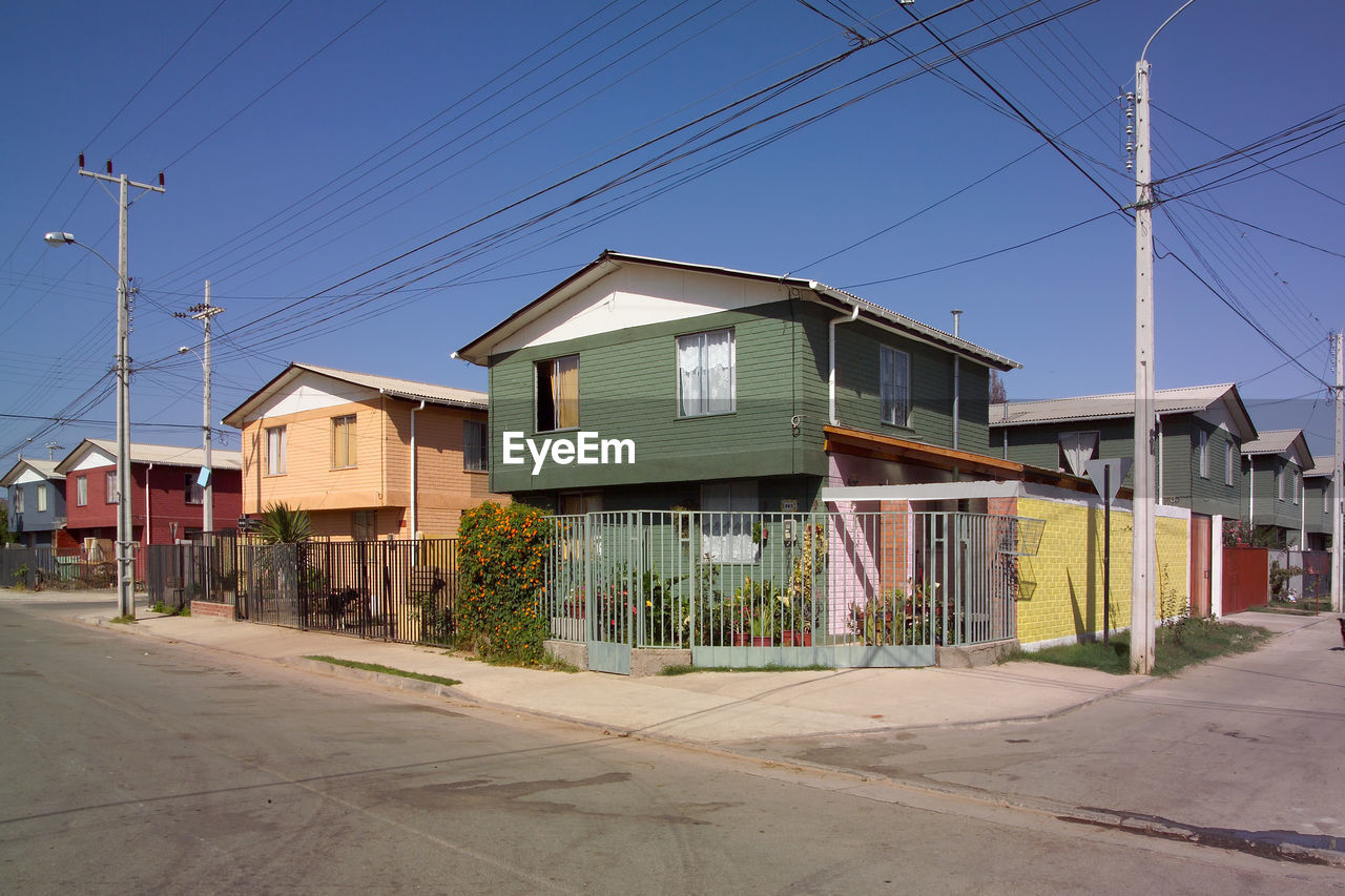 architecture, residential area, neighbourhood, built structure, building exterior, town, suburb, building, house, sky, street, city, residential district, cable, electricity, road, nature, no people, clear sky, urban area, technology, blue, transportation, power line, outdoors, day, downtown, home, real estate, industry, facade, electrical supply
